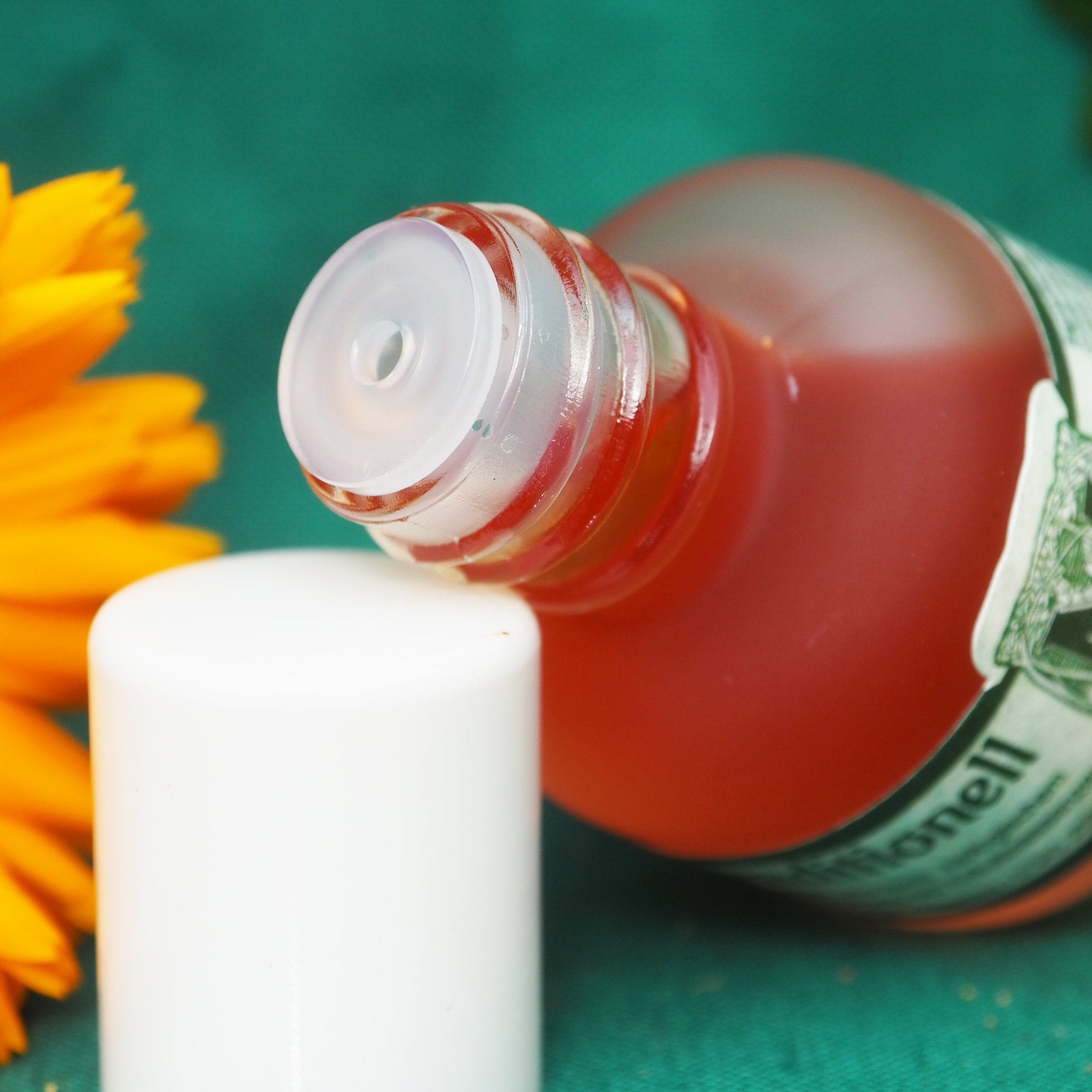 Massageöl traditionel 15ml geöffnet, Trofeinsatz sichtbar, im HIntergrund eine gelbe Blume